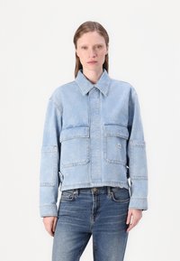 Veste en denim bleu clair avec un col, deux poches avant et un design cropped. Tissu texturé avec des détails de couture visibles.