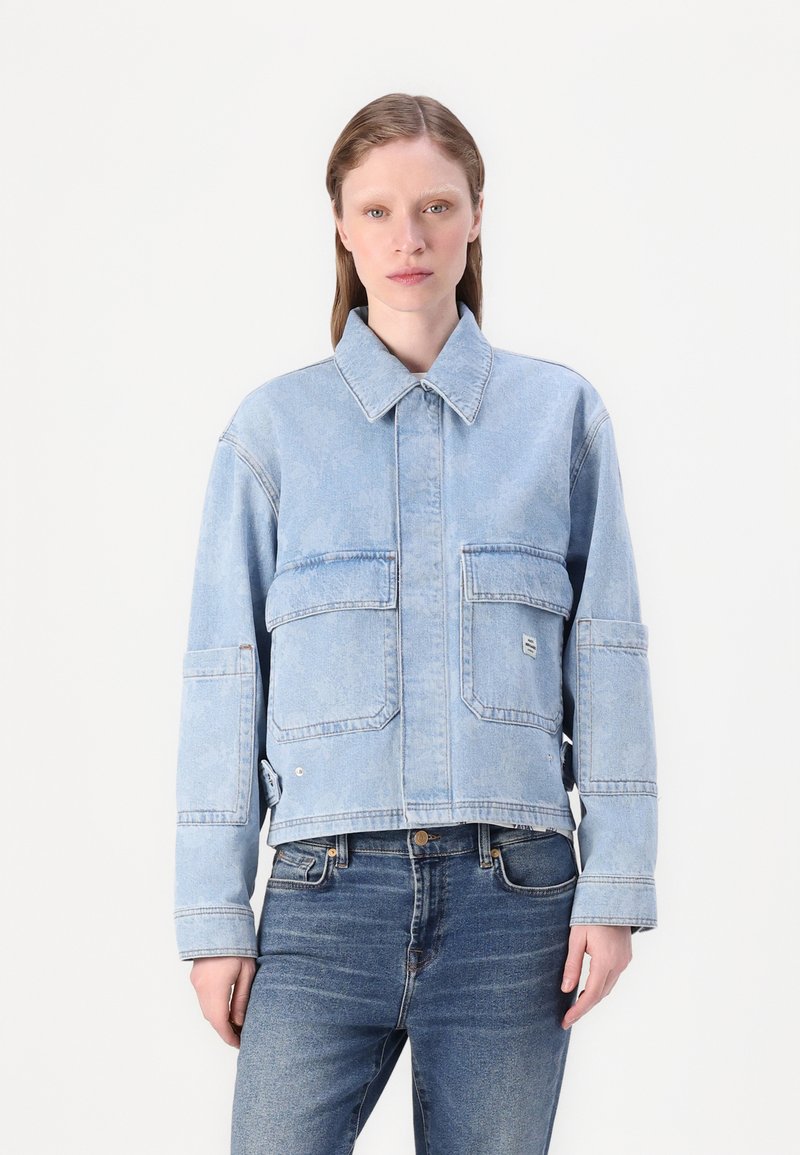 Veste en denim bleu clair avec un col, deux poches avant et un design cropped. Tissu texturé avec des détails de couture visibles.