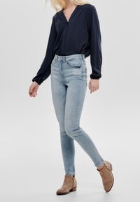 Blouse marine avec fermeture à boutons, jean skinny bleu clair, et bottines marron clair. Tissu lisse et coupe ajustée avec jambes fuselées.