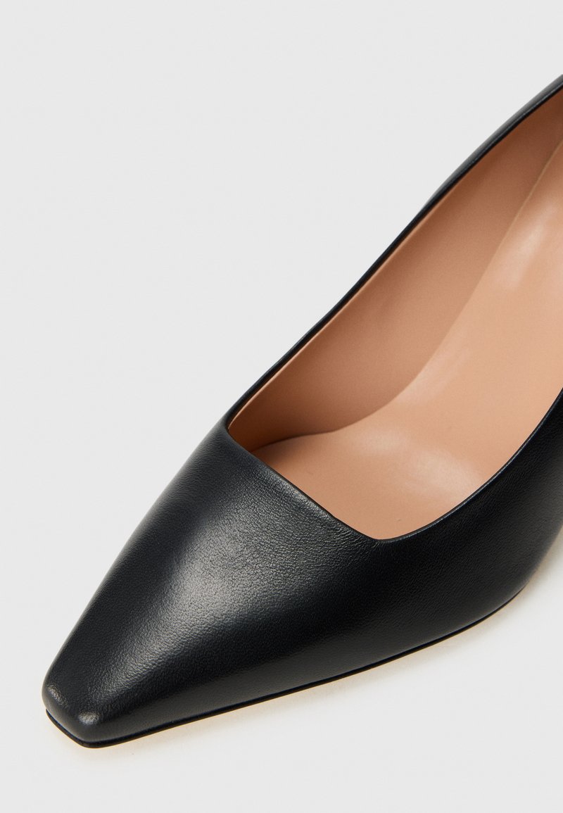 Czarne skórzane szpilki z ostrym noskiem i gładką fakturą, z wycięciem odsłaniającym beżową wkładkę.
