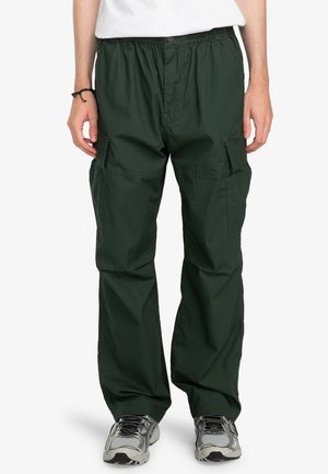 Grüne Cargo-Hosen mit lockerem Schnitt, elastischem Bund und mehreren Taschen, aus leichtem Stoff gefertigt. Getragen mit grauen Sportschuhen.