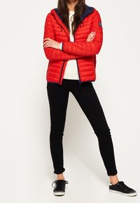 Czerwona pikowana kurtka puchowa z kapturem, granatowymi akcentami, przednim zamkiem błyskawicznym i bocznymi kieszeniami. Do tego czarne obcisłe jeansy i czarne sneakersy.