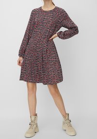 Květinové šaty s námořnickým pozadím, zdobené červenými a modrými rozptýlenými vzory, dlouhými rukávy a rozšířeným střihem, doplněné béžovými kotníkovými botami.