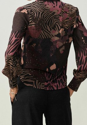 Blouse noire et violette à motifs avec différents imprimés animaliers texturés et manches longues. Le tissu semble léger et semi-transparent.