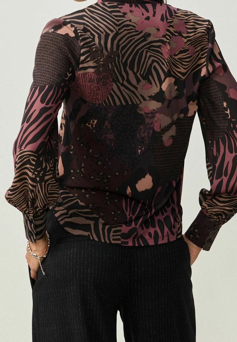 Blouse noire et violette à motifs avec différents imprimés animaliers texturés et manches longues. Le tissu semble léger et semi-transparent.