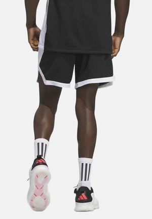 Homme portant un short de sport noir avec des bordures blanches, des chaussettes blanches mi-mollet avec des rayures noires, et des baskets noires et blanches avec des accents rouges.