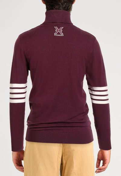 Maglione bordeaux con colletto alto, caratterizzato da strisce orizzontali bianche sulle maniche e un piccolo logo sul retro. Tessuto morbido e liscio.
