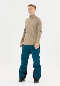 Lichtbruine lange mouw top met een half-rits kraag gecombineerd met teal broek met zwarte accenten en een verstelbare taille. Lichtgewicht, zachte textuur.