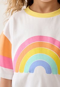 Valge puuvillane T-särk, millel on mitmevärviline vikerkaare graafika roosa, oranži, kollase ja sinise värviga; kontrastsest kollasest kaelus ja värvilised varrukad.