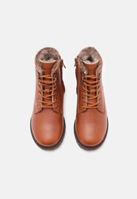 Une paire de bottes en cuir marron à lacets avec doublure en fourrure et fermetures éclair sur les côtés, vues de dessus sur un fond blanc.