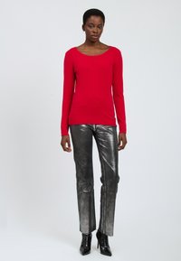 Maglione rosso a maniche lunghe con scollo rotondo, abbinato a pantaloni aderenti argentati e scarpe con tacco nere. Texture liscia in tutto.