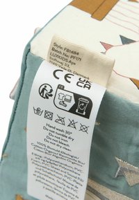 Étiquette de vêtement indiquant les instructions de lavage, la composition du matériau et les marques de conformité CE UKCA sur un tissu à motifs d'étoiles.