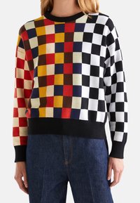 Färgglad stickad tröja med ett schackbrädesmönster i rött, gult, svart, vitt och blått, med en svart ribbad halsringning och fåll.