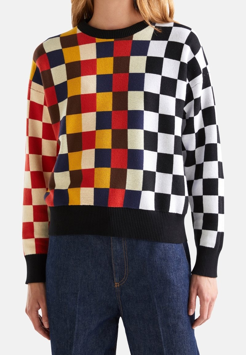 Färgglad stickad tröja med ett schackbrädesmönster i rött, gult, svart, vitt och blått, med en svart ribbad halsringning och fåll.