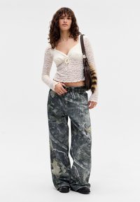 Hvit blonde langermet topp med knyting foran, parret med løse grå camo-mønstrede jeans og chunky svarte sko, bærende en brun veske.