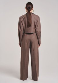 Bruin op maat gemaakte twee-delige pak met een cropped jasje met gestructureerde schouders en wijde broek met plooien, gemaakt van textuurstof.