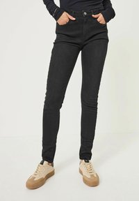 Czarne rurki z wysokim stanem, wykonane z denimu, z klasycznym pięcio-kieszeniowym fasonem i minimalnym przeszyciem. Trampki w kolorze tan z sznurówkami.