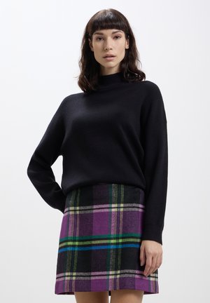 Maglione nero con collo alto e maniche lunghe, abbinato a una mini gonna a quadri viola con righe verdi e blu.