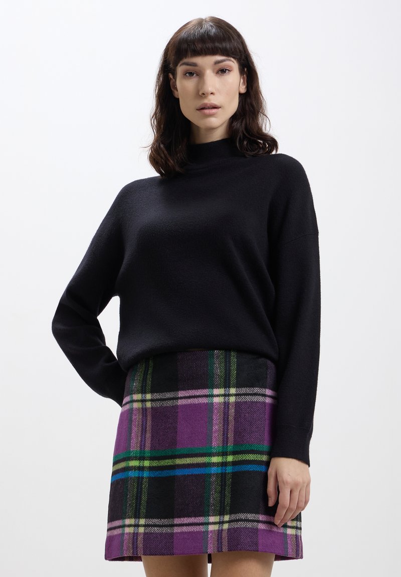 Maglione nero con collo alto e maniche lunghe, abbinato a una mini gonna a quadri viola con righe verdi e blu.