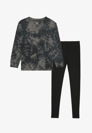 Tumehallide ümarate mustritega pika varrukaga tie-dye särk, millele on sobitatud mustad retuusid ja roosa-valge mustriga sokid.