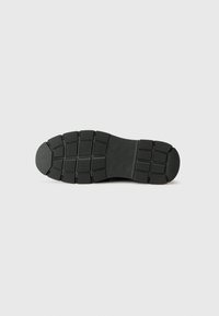 Suola di scarpa in gomma nera con superficie testurizzata e modanata; presenta vari rilievi e scanalature per aderenza e trazione.
