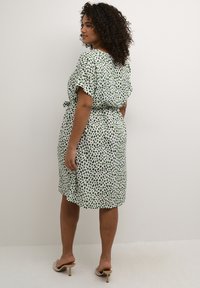Vestido de patrón verde y blanco con mangas cortas, cintura con cinturón, y un dobladillo a la altura de la rodilla, hecho de un tejido ligero con una textura suave.