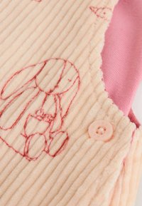 Lichtroze ribbelstof met een rode geborduurde konijn en een bijpassende roze knoop op een kledingstuk.