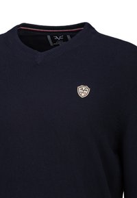 Marineblauer V-Ausschnitt-Pullover mit dünnem, gestreiftem Kragen und kleinem, gesticktem Schild-Logo auf der Brust. Weiche Strickstofftextur.