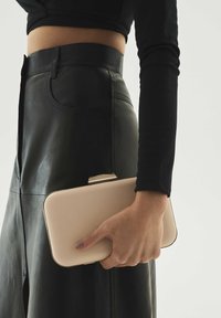 Bordinis stačiakampis delninukas su lygia odine išore ir metaline sagtimi, laikomas rankoje šalia juodos odinės sijono.