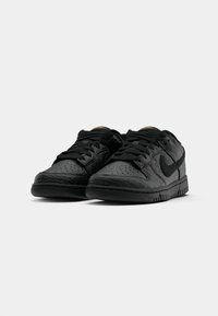 Juodi Nike sportbačiai su tekstūruotu paviršiumi, perforuotu pirštų skyriumi, juodais raišteliais ir juoda Swoosh logotipu. Lygus padas ir elegantiškas dizainas.