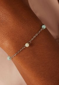 Zilveren schakelarmband met twee ronde kralen: een lichtblauwe en een opaak witte, tegen een gestructureerde huid.
