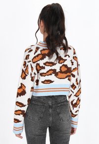 Korte trui in het wit met een bruin dierenprint, voorzien van een lichtblauwe ribgebreide kraag en manchetten, met contrasterende oranje strepen aan de onderrand.