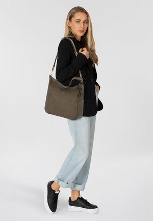 Borsa a spalla in suede verde oliva con forma arrotondata, caratterizzata da un accento con nappina, bordi beige e una tracolla removibile.