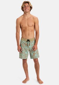 Bañador en un patrón de marrón claro y verde azulado que presenta foliaje tropical. Confeccionado en tela ligera, con cintura con cordón y sin bolsillos.