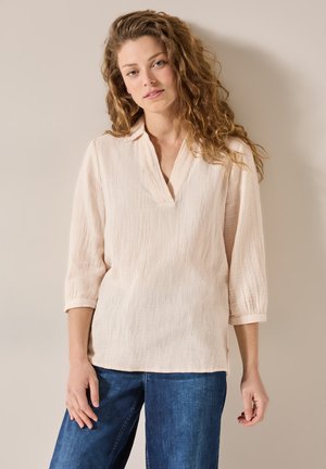 Blouse en coton texturé rose clair avec un col en V et des manches trois-quarts, assortie à un jean en denim large bleu.