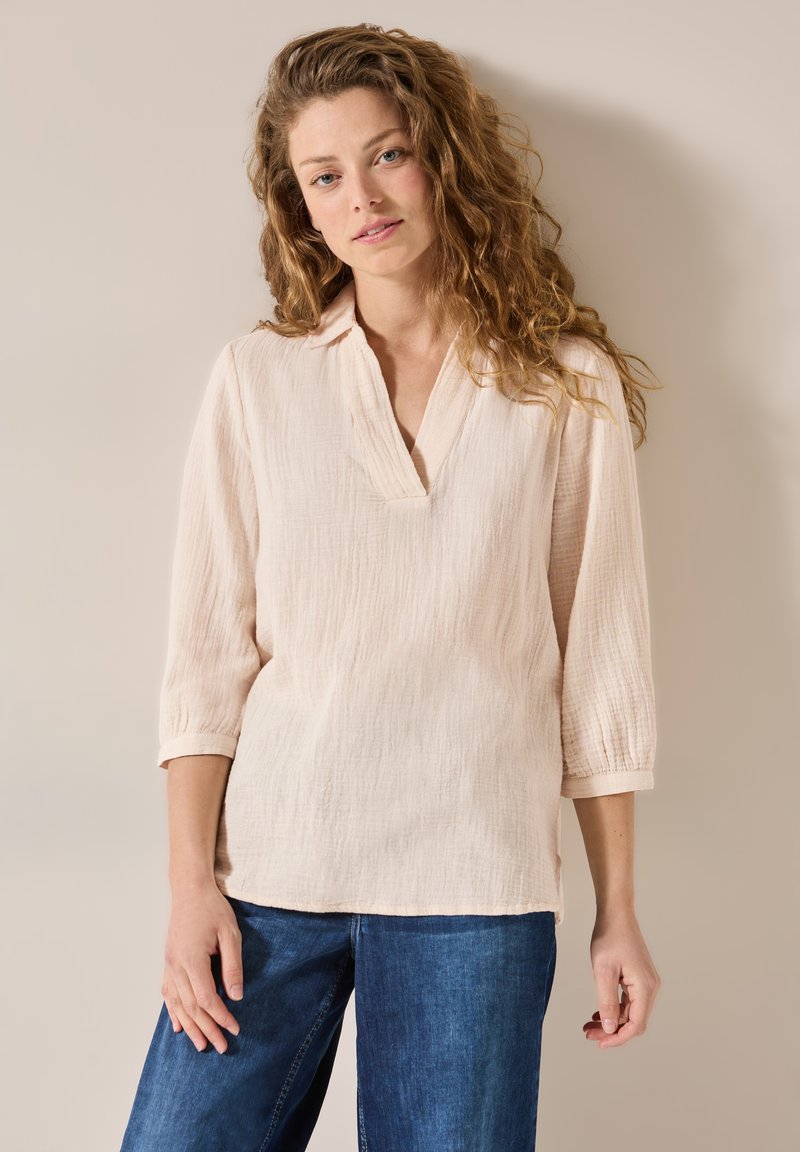Blouse en coton texturé rose clair avec un col en V et des manches trois-quarts, assortie à un jean en denim large bleu.