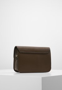 Brun læderhåndtaske med flaplukning, der har en glat tekstur og minimalistisk design. Sidehardwaredetalje fuldender udseendet.