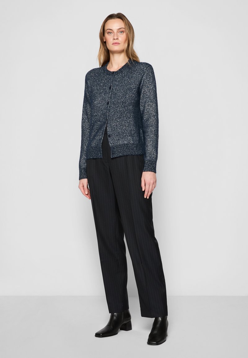 Marineblau gestrickte Strickjacke mit strukturiertem Finish, rundem Ausschnitt, vorderen Knöpfen und gerippten Bündchen, kombiniert mit schwarzen Nadelstreifenhosen und Stiefeletten.