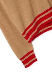 Manga y dobladillo de suéter de punto beige con puños acanalados a rayas rojas y beige sobre un fondo blanco.