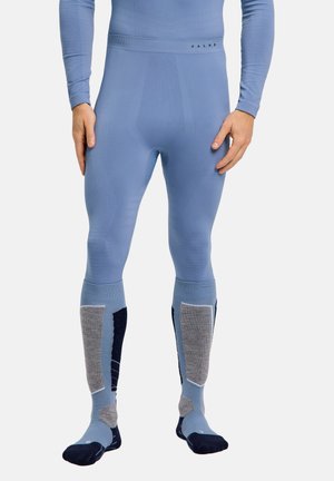 Man wearing fitted blue long underwear pants with integrated knee and foot sections in gray and dark blue accents.