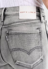 Jeans de mezclilla gris con un parche distintivo que dice "Levi's Line 8". Presenta un diseño de cinco bolsillos y detalles de costura prominentes.