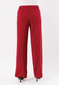Pantaloni rossi a vita alta con design a gamba larga, realizzati in un tessuto morbido; presentano passanti per cintura e due tasche posteriori.