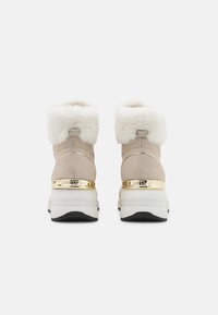 Bottines beiges avec des dessus en fourrure, texture perforée, accent doré autour du talon, et semelle épaisse blanche avec un fond noir.