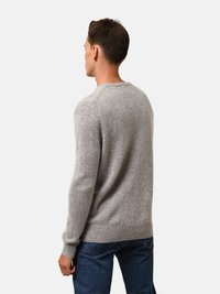 Grauer Strickpullover mit gerippten Bündchen und Saum, ausgestattet mit einem Rundhalsausschnitt und einer strukturierten Oberfläche. Wird über blauen Jeans getragen und zeigt ein einfaches Design.