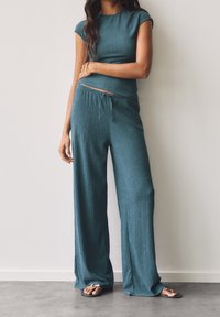 Ensemble deux pièces en tricot bleu sarcelle avec un haut moulant à manches courtes et un pantalon ample à jambes larges. Tissu texturé avec détail de cordon à la taille.