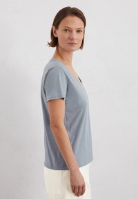 Jasnoniebieska koszulka polo z krótkim rękawem i dekoltem w serek, wykonana z miękkiego materiału, o dopasowanym kroju i minimalnych szwach.