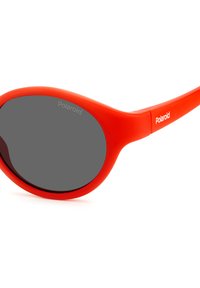 Occhiali da sole rossi in plastica con lenti ovali, tonalità grigia e finitura opaca liscia. Presentano il marchio "Polaroid" sulla tempia.