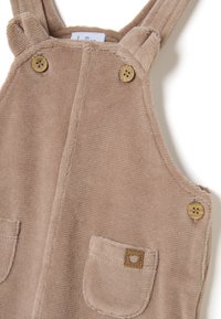Braune Corduroy-Overall mit zwei Vordertaschen, Holzknöpfen und gesticktem Etikett. Strukturierter Stoff, verstellbare Träger und runder Ausschnitt.