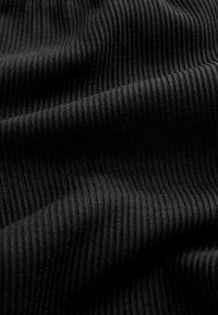 Nahaufnahme eines schwarzen gerippten Stoffes mit feinen vertikalen Linien und weichen Falten, die Textur und Strickmuster hervorheben.