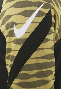 Nike sportkläder med ett mönster av gula och svarta tigerstrimmor, med en vit logotyp och svarta detaljer på axeln.